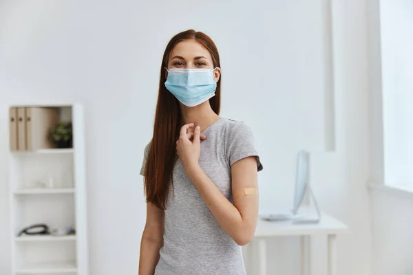 Ung kvinna på sjukhus bär en medicinsk mask med en bakteriedödande plåster på axeln säkerhet immunisering — Stockfoto