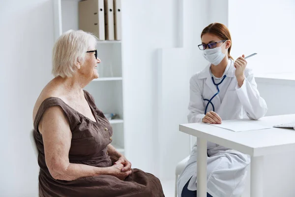 Läkare på läkarmottagningen pratar med en äldre kvinna hälsovård — Stockfoto