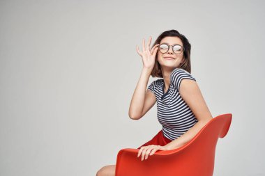 Kırmızı sandalyede oturan şık elbiseli güzel kadın stüdyoda poz veriyor.