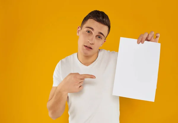 Een man in een wit t-shirt vel papier reclame kopiëren ruimte gele achtergrond — Stockfoto