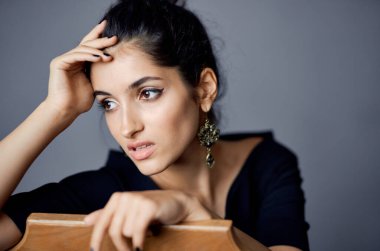 Güzel kadın mücevher takıyor. Sandalyenin yanında poz veriyor. Siyah elbise yaşam tarzı stüdyosu.