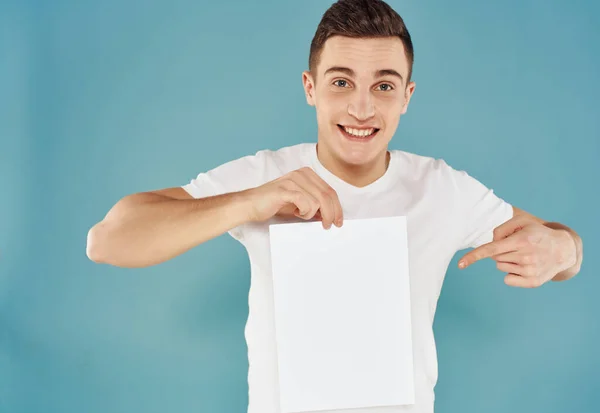 Cheerful man in white t-shirt with a sheet of paper Copy Space Studio isolated background