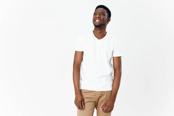 Happy african man in white t-shirt and beige pants on light background cropped view — Stock Photo, Image