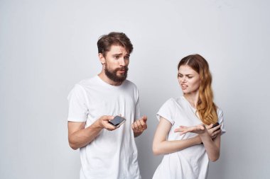 Beyaz tişörtlü, ellerinde telefonlar olan genç bir çift arka planlarını aydınlatıyor.