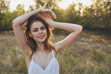 Yeşil çim tarlasında yürüyen beyaz elbiseli neşeli güzel kadın.
