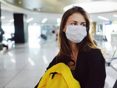 Tıbbi maske takan sarı sırt çantalı bir yolcu havaalanında oturuyor.