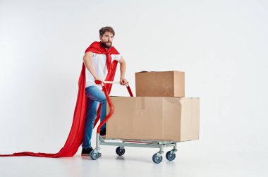 Kırmızı pelerinli sakallı adam. Arka planda kutu ışığı olan bir nakliye aracı.