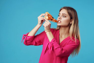 Pembe tişörtlü kadın elinde pizzayla abur cuburu yakın plan çekiyor.