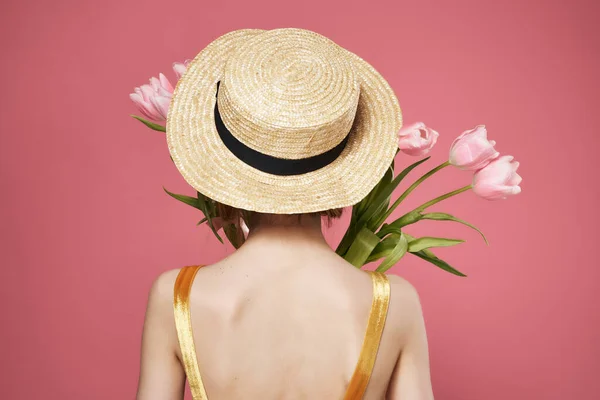 Mulher em um chapéu com um buquê de flores fica para trás fundo rosa — Fotografia de Stock