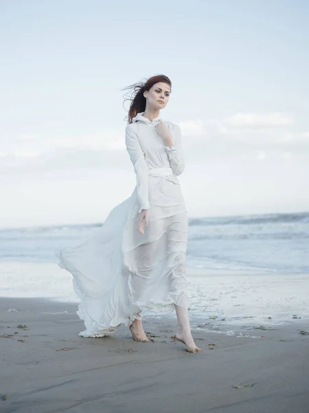 Μια γυναίκα με λευκό φόρεμα περπατά κατά μήκος της ακτής του ωκεανού Ελευθερία πολυτέλεια — Φωτογραφία Αρχείου