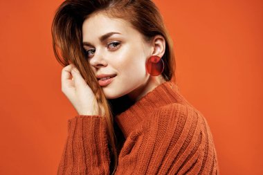 Kızıl saçlı, kırmızı kazaklı, küpeli, yakın plan mücevherli bir kadın.