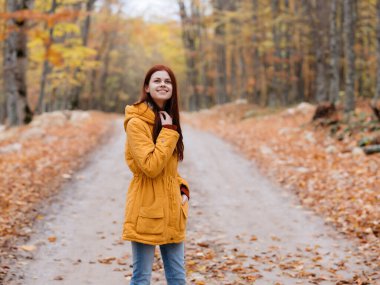 Sarı ceketli kadın sonbaharda orman yolculuğu yapar.