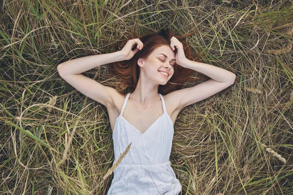 Alegre pelirroja mujer en un vestido blanco se encuentra en el descanso hierba aire fresco —  Fotos de Stock