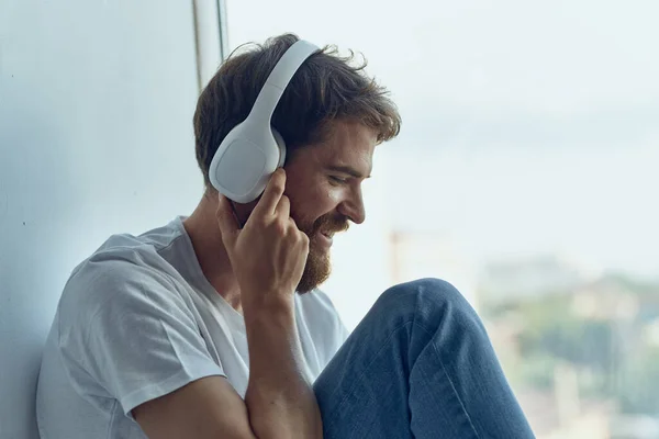 Homme barbu assis près de la fenêtre dans les écouteurs écouter de la musique — Photo