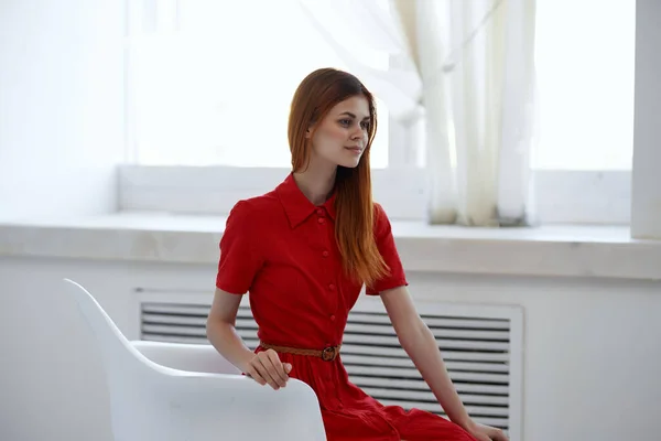 빨간 드레스를 입은 예쁜 여자가 창가에 앉아 있는 모습 — 스톡 사진