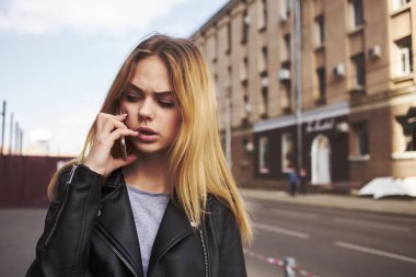 Güneş gözlüklü şık bir kadın sokakta telefonla konuşuyor.