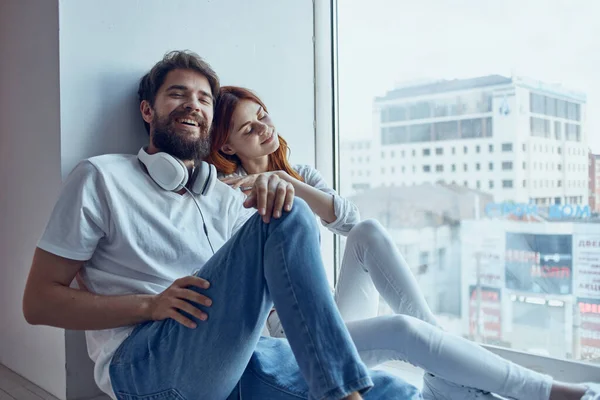 Ein junges Paar sitzt mit Kopfhörern am Fenster — Stockfoto