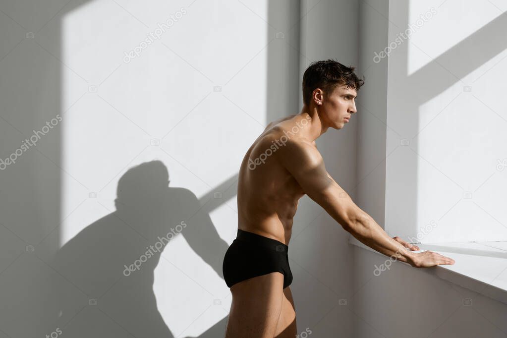 male bodybuilder in black shorts posing near the window