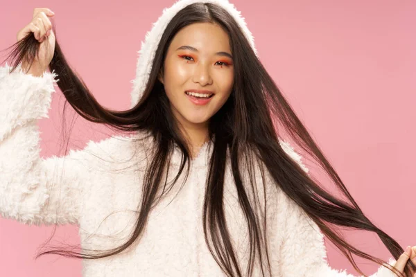 Retrato de una mujer asiática con cabello oscuro en un suéter blanco con una capucha sobre un fondo rosa — Foto de Stock