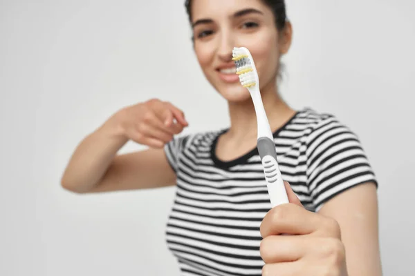 Brunette in a striped t-shirt toothbrush in hand light background — Stock Photo, Image