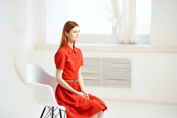 Mulher em vestido vermelho senta-se em uma cadeira perto do modelo da janela — Fotografia de Stock