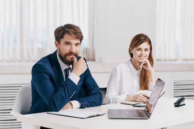 Erkek ve kadın yöneticiler dizüstü bilgisayar teknolojisinin önünde masada oturuyorlar.