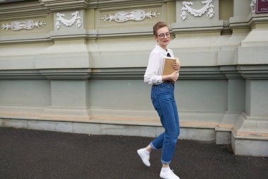 Gözlüklü bir öğrenci kitap iletişimiyle şehirde dolaşıyor.