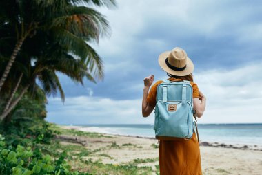 Sırt çantalı, şapkalı, kumsal adasında uzun ağaçlı bir kadın.