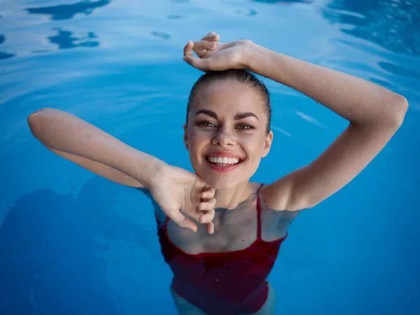 Mulher alegre nada na piscina e um sorriso de maiô vermelho — Fotografia de Stock