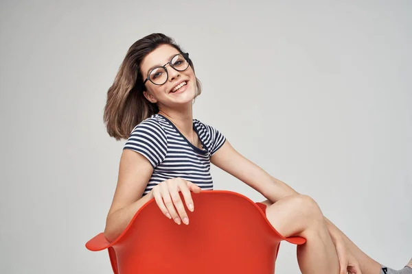 Kvinna med glasögon sitter på den röda stolen ljus bakgrund Livsstil — Stockfoto