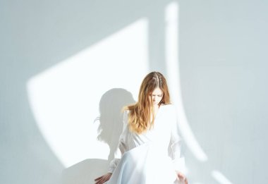 Duvara yaslanmış beyaz elbiseli bir kadın yalnız bir arka plan aşkı yaşıyor.