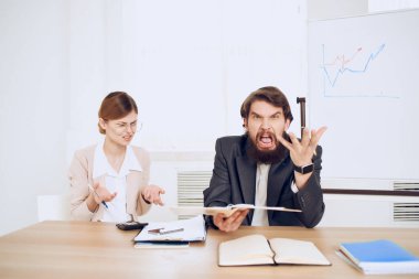 İş adamı ve kadın çalışma masasında oturmuş tatminsiz iletişim duyguları haykırıyorlar.