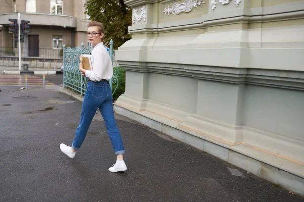 Pretty woman with short hair is walking down the street with a book in her hands — Stock Photo, Image