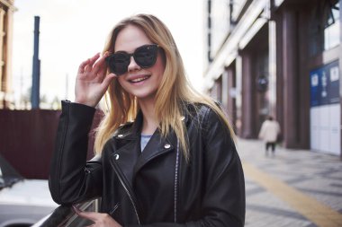 Güneş gözlüklü tatlı sarışın sokakta yürüyor.