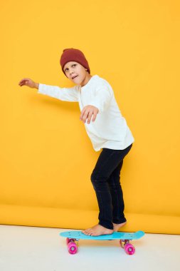 Kırmızı sırt çantası, mavi kaykay, sarı arka plan, havalı gülümseyen çocuk.