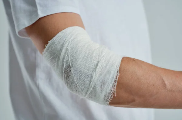 Paciente masculino con una camiseta blanca con un fondo aislado de la mano vendado —  Fotos de Stock