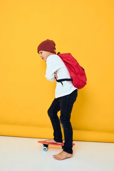 赤いバックパックを持つ可愛い男の子の肖像｜赤いスケートボード隔離された背景 — ストック写真