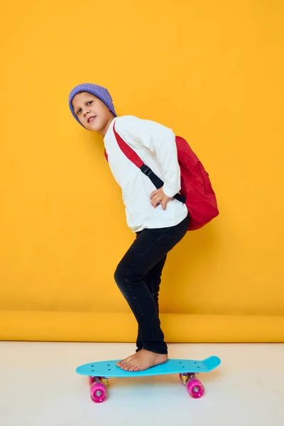 Glada liten unge med röd ryggsäck blå skateboard isolerad bakgrund — Stockfoto