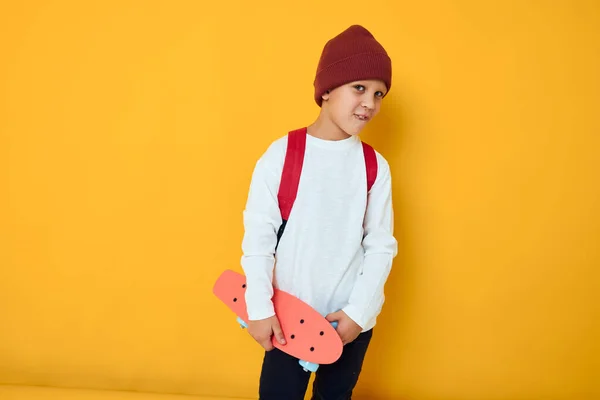 Glad skolpojke med röd ryggsäck röd skateboard gul färg bakgrund — Stockfoto