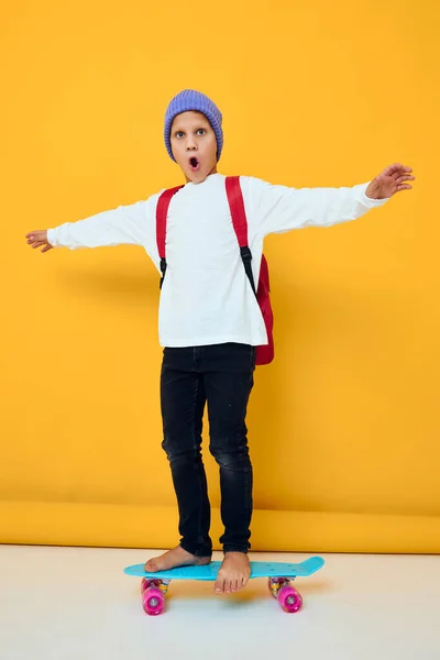 Улыбающийся школьник катается на скейтборде в синей шляпе — стоковое фото