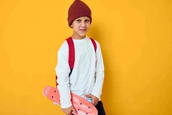 손에는 빨간 모자 스케이트 보드를 단 멋진 미소짓는 소년 이 외진 배경을 가지고 있다 — 스톡 사진