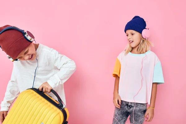 헤드폰 스튜디오 포즈를 취하고 있는 한 소녀와 소년의 노란 여행 가방의 모습 — 스톡 사진