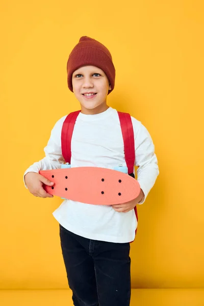 Glad skolpojke i en röd hatt skateboard i händerna isolerad bakgrund — Stockfoto