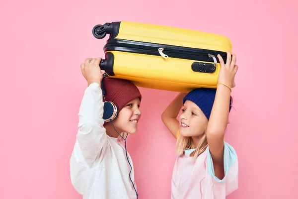 분홍색 배경으로 손에 노란 가방을 들고 있는 즐거운 소년 소녀 — 스톡 사진