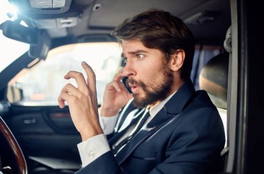 Arabada takım elbiseli sakallı bir adam işe telefonla gidiyor.