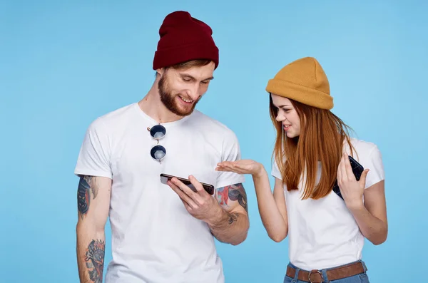 Jovem casal em chapéus com telefones em mãos comunicação de moda — Fotografia de Stock