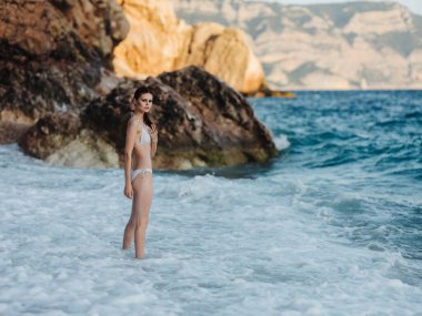 Beyaz mayo giymiş bir kadın sahilde yürür, okyanus geçer.