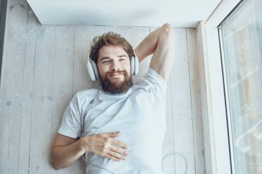 Kulaklık teknolojisi olan genç bir adam pencerenin yanında yatıyor.