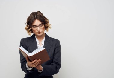 İş elbiseli bir kadın, elinde bir kitapla arka planı aydınlatmış.