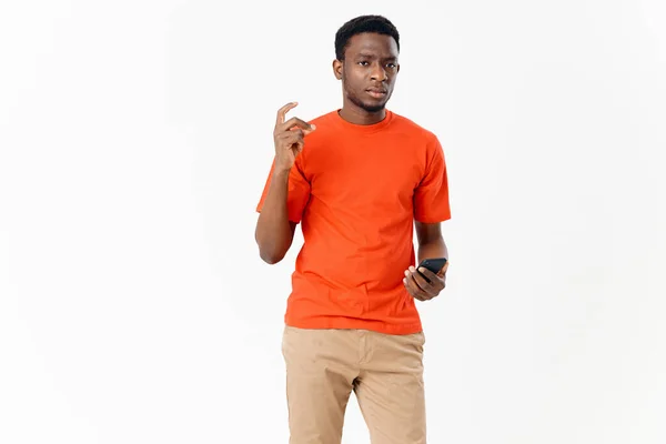 Bonito afro-americano em uma t-shirt e shorts com um celular em um fundo leve — Fotografia de Stock